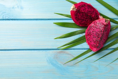 Delicious cut red pitahaya fruit and palm leaf on light blue wooden table, flat lay. Space for text