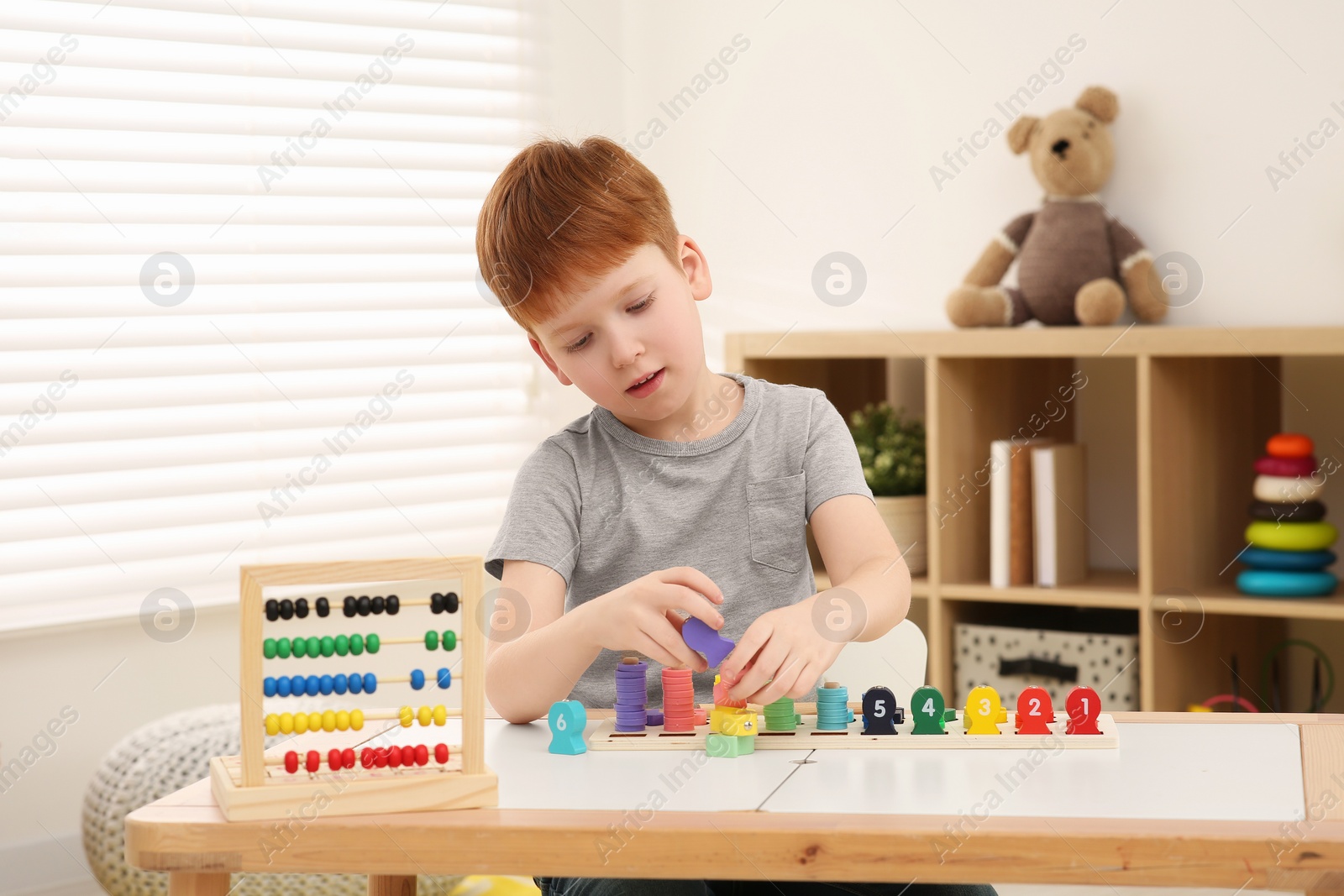 Photo of Little boy playing with Educational game Fishing for Numbers at desk in room. Learning mathematics with fun