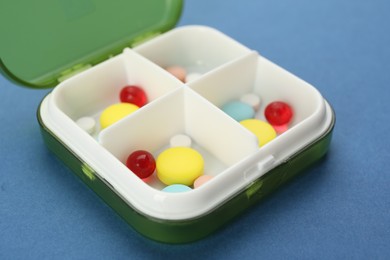 Photo of Plastic box with different pills on blue background, closeup