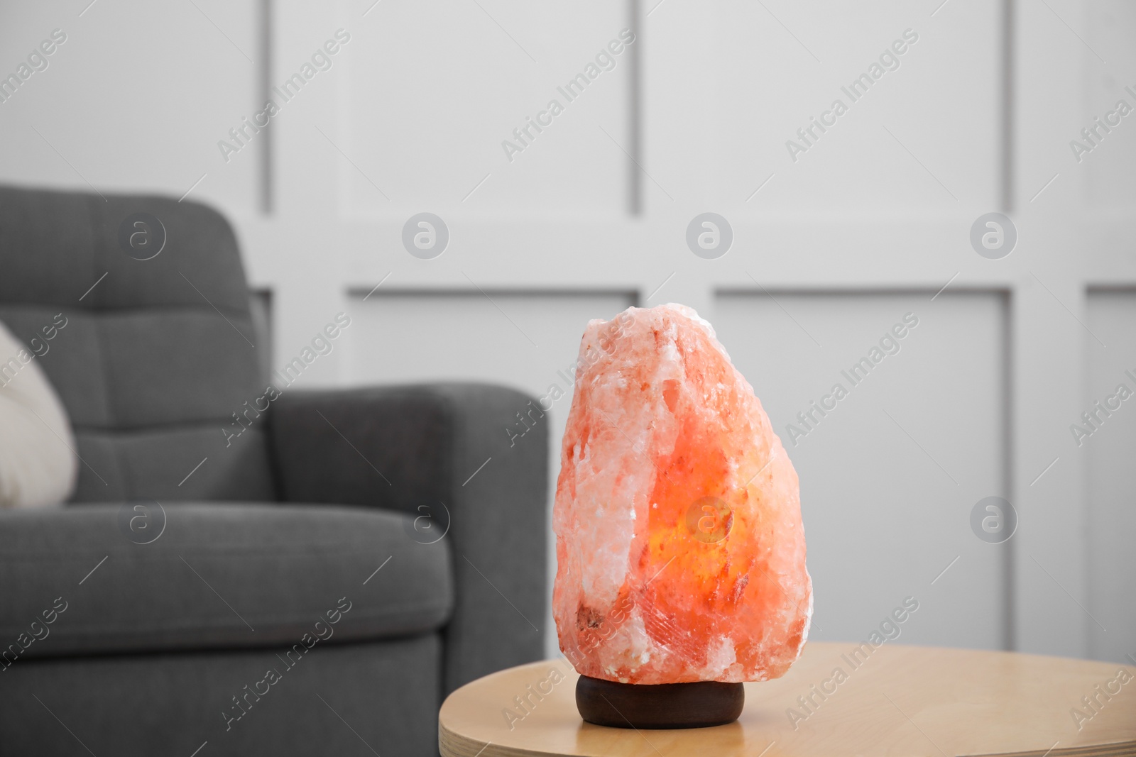 Photo of Himalayan salt lamp on wooden table near sofa indoors