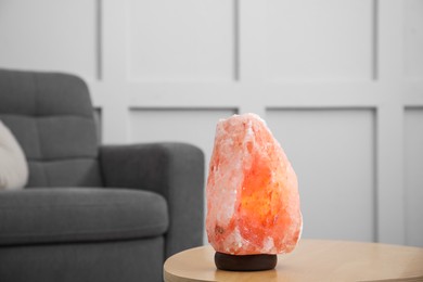 Photo of Himalayan salt lamp on wooden table near sofa indoors