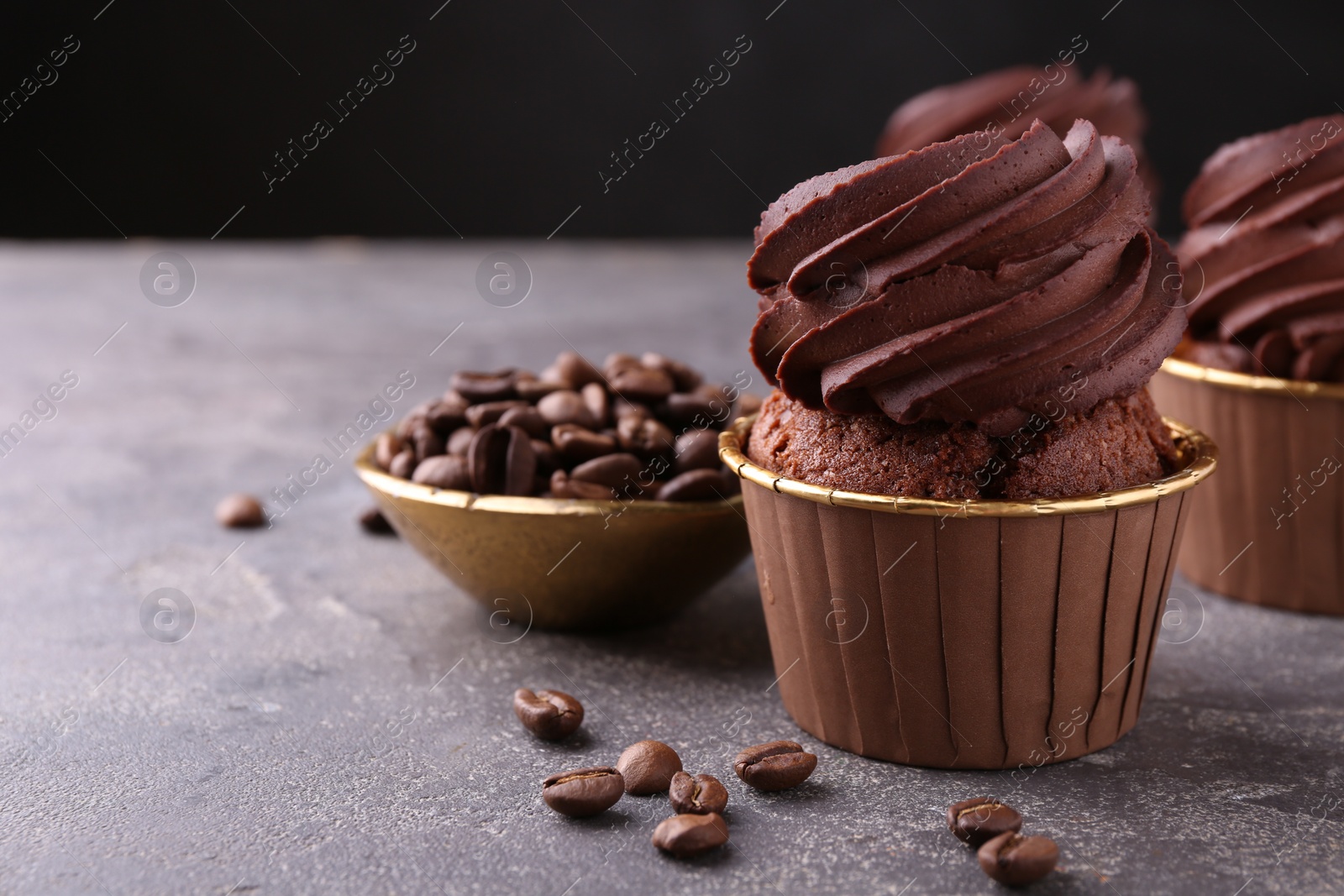 Photo of Delicious chocolate cupcakes and coffee beans on grey textured table, closeup. Space for text