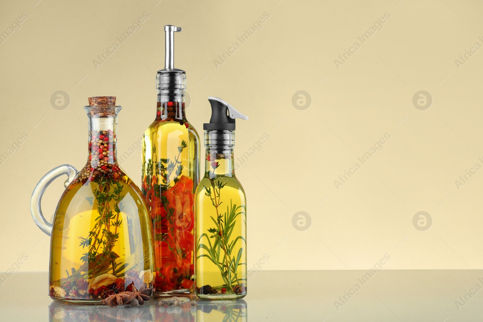 Photo of Cooking oil with different spices and herbs in bottles on beige table. Space for text