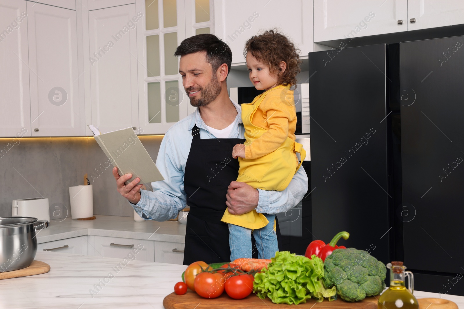 Photo of Cute little girl and her father with recipe book cooking in kitchen