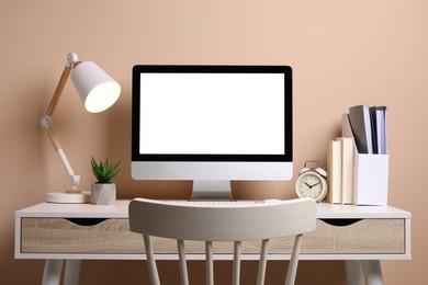 Photo of Cozy workspace with computer, lamp, houseplant and stationery on wooden desk