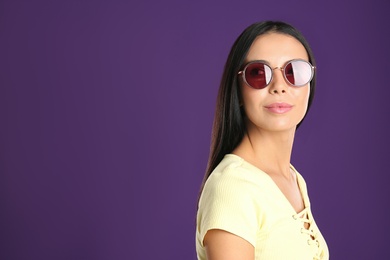 Photo of Beautiful woman wearing sunglasses on purple background. Space for text