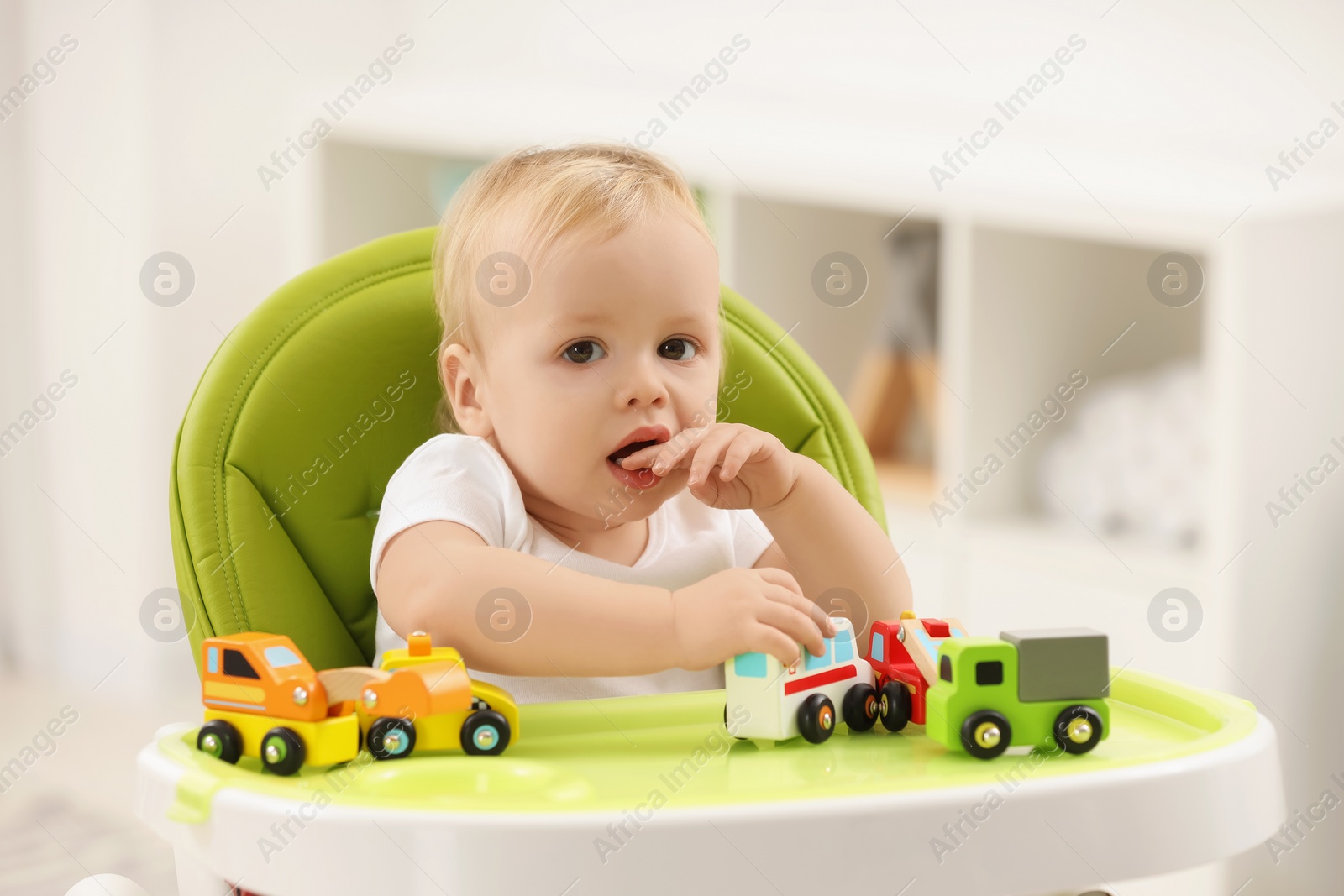 Photo of Children toys. Cute little boy playing with toy cars in high chair at home