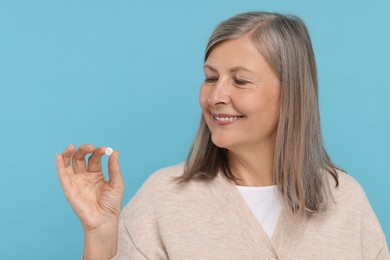 Photo of Senior woman with pill on light blue background