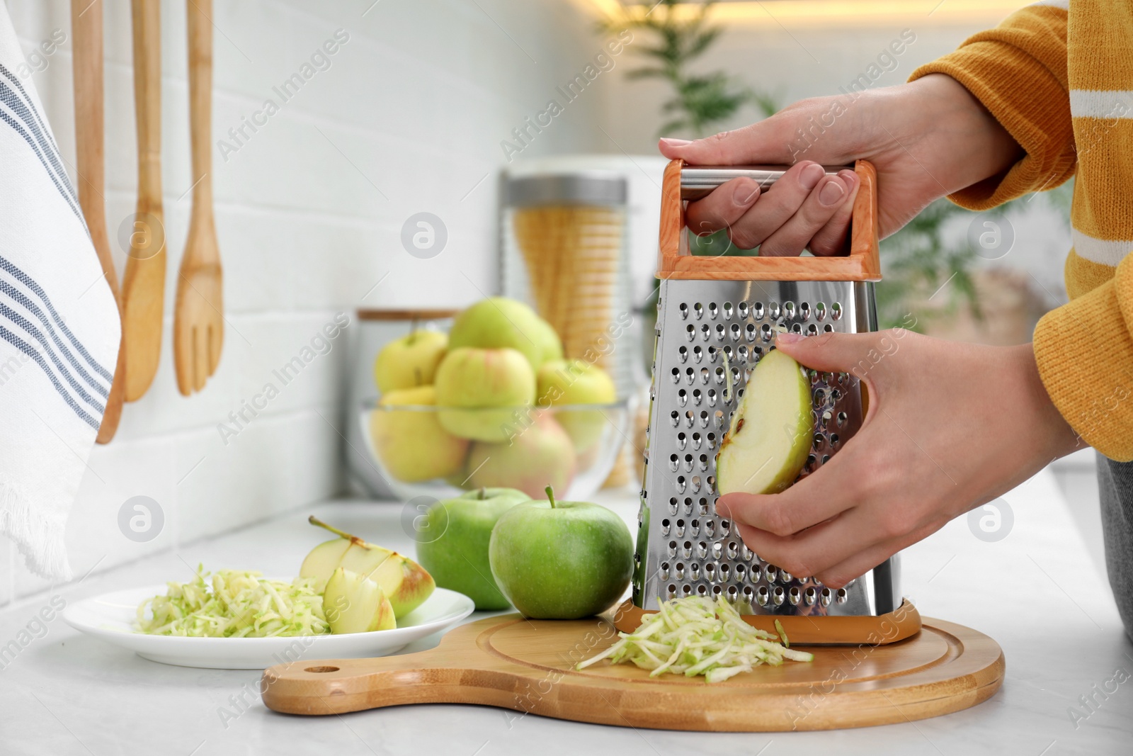 Photo of Woman grating fresh green apple at kitchen counter, closeup