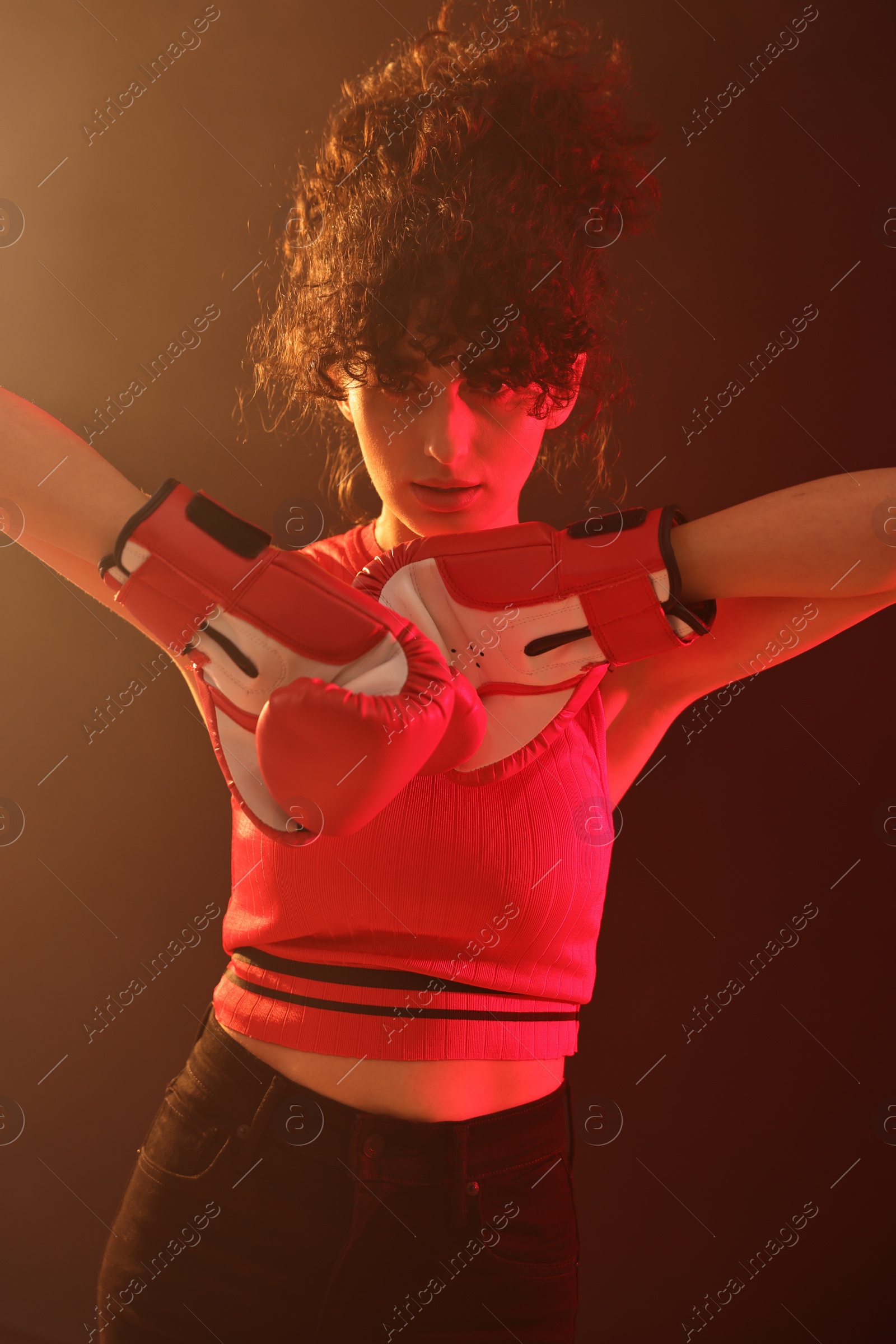 Photo of Beautiful young woman with boxing gloves on color background in neon lights