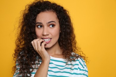 Photo of African-American woman biting her nails on yellow background