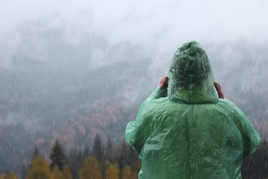 Photo of Woman in raincoat enjoying mountain landscape under rain, back view