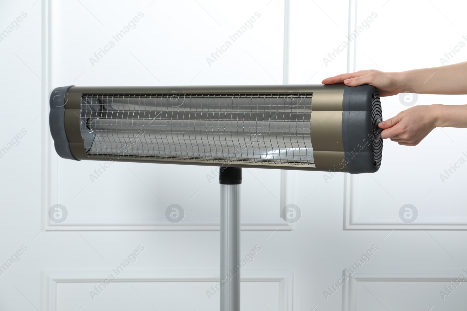 Photo of Young woman adjusting temperature on modern electric infrared heater near white wall, closeup