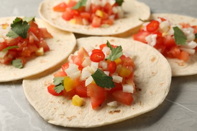 Photo of Delicious tacos with vegetables and parsley on grey marble table, closeup