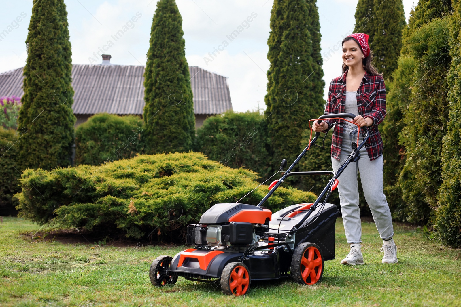 Photo of Smiling woman cutting green grass with lawn mower in garden