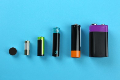 Different types of batteries on turquoise background, flat lay