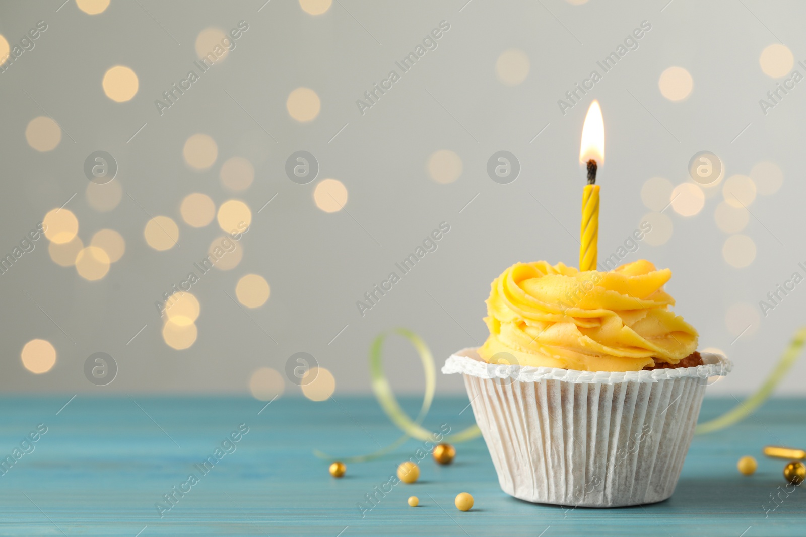 Photo of Tasty birthday cupcake on light blue wooden table against blurred lights. Space for text