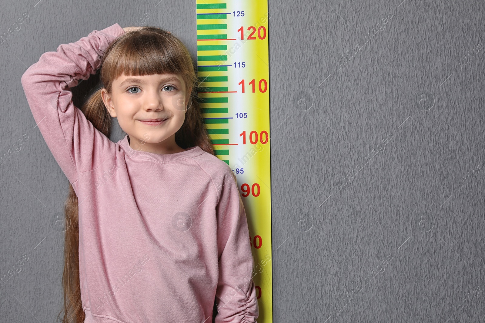 Photo of Little girl measuring her height on grey background
