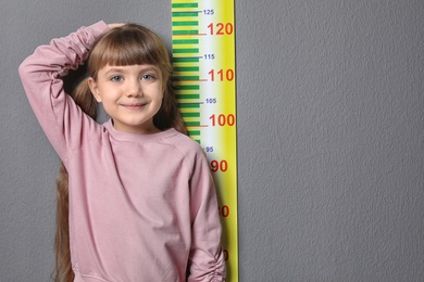 Little girl measuring her height on grey background