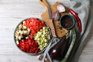 Cooking delicious ratatouille. Fresh ripe vegetables, plate and knife on white wooden table, flat lay