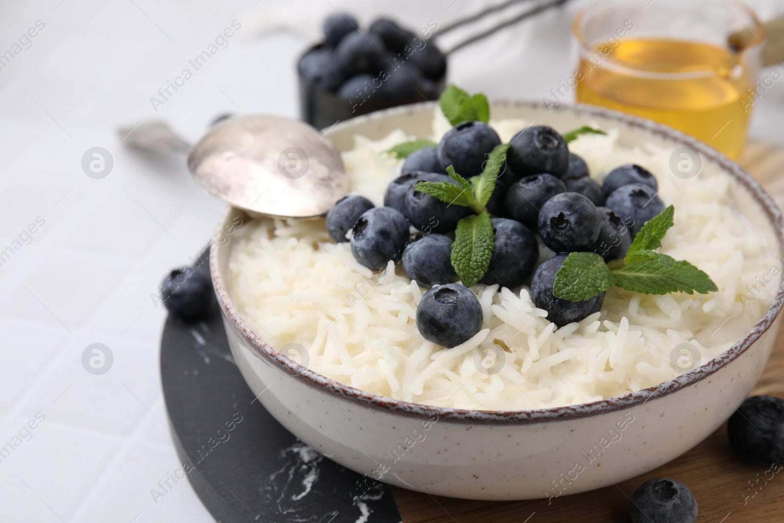 Photo of Bowl of delicious rice porridge with blueberries and mint served on table, closeup