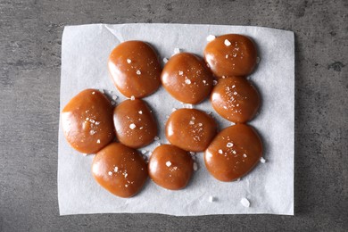 Photo of Tasty caramel candies and salt on grey table, top view