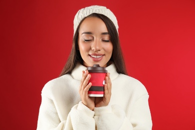 Photo of Happy beautiful woman with paper cup of mulled wine on red background