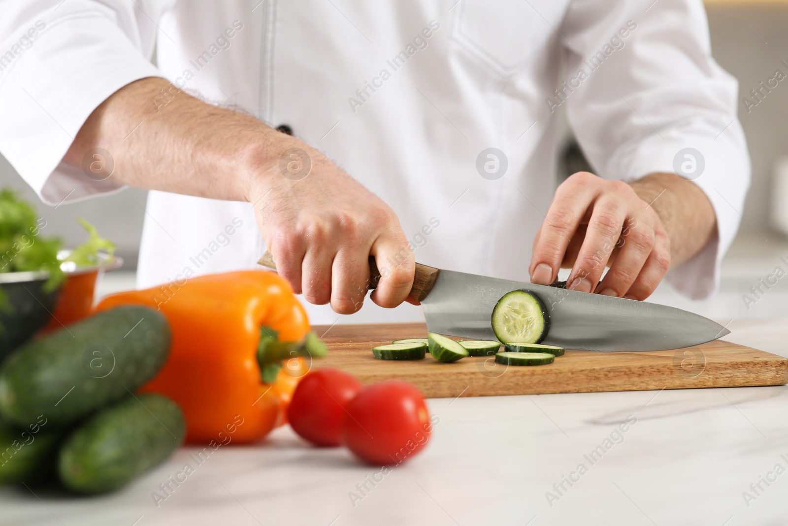 Photo of Chef cutting cucumber at marble table in kitchen, closeup