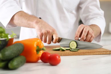 Photo of Chef cutting cucumber at marble table in kitchen, closeup