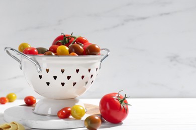 Photo of Metal colander with fresh tomatoes on white wooden table, space for text