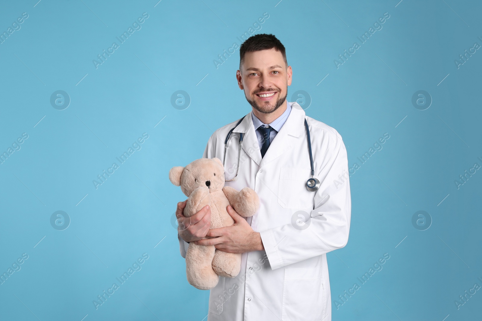 Photo of Pediatrician with teddy bear and stethoscope on light blue background