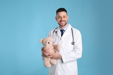 Pediatrician with teddy bear and stethoscope on light blue background