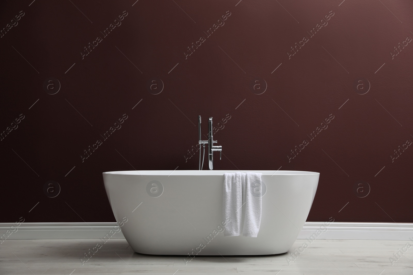 Photo of Modern ceramic bathtub with towel near burgundy wall indoors