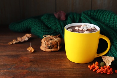 Photo of Cup of hot drink and knitted sweater on wooden table, space for text. Cozy autumn atmosphere