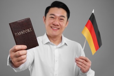 Photo of Immigration. Happy man with passport and flag of Germany on grey background, selective focus
