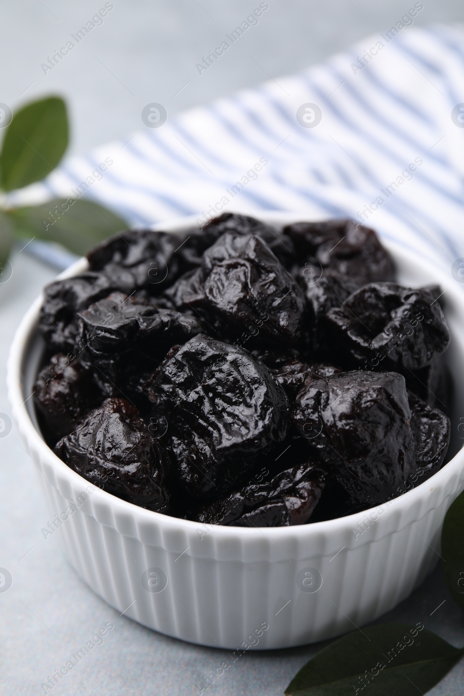 Photo of Sweet dried prunes in bowl on light grey table, closeup