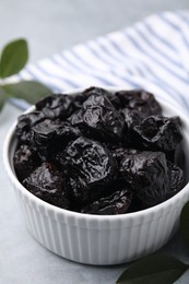 Sweet dried prunes in bowl on light grey table, closeup