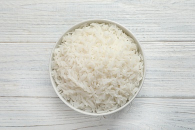 Photo of Bowl of tasty cooked rice on white wooden background, top view