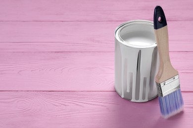 Photo of Can of white paint and brush on pink wooden table, space for text