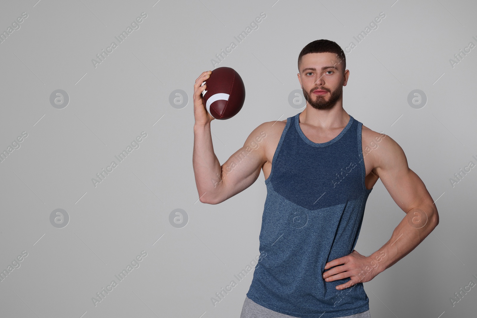 Photo of Athletic young man with American football ball on light grey background. Space for text