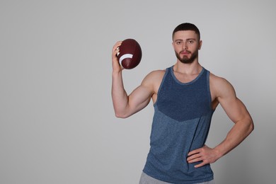 Athletic young man with American football ball on light grey background. Space for text