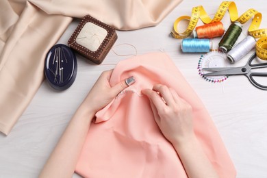 Photo of Woman with sewing needle and thread embroidering on cloth at white wooden table, top view