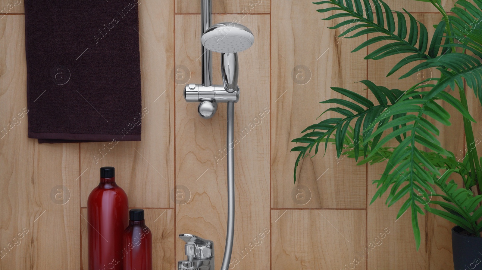 Photo of Brown soft towel near showerhead on tiled wall in bathroom