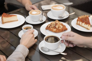 Friends drinking coffee at wooden table in outdoor cafe, closeup