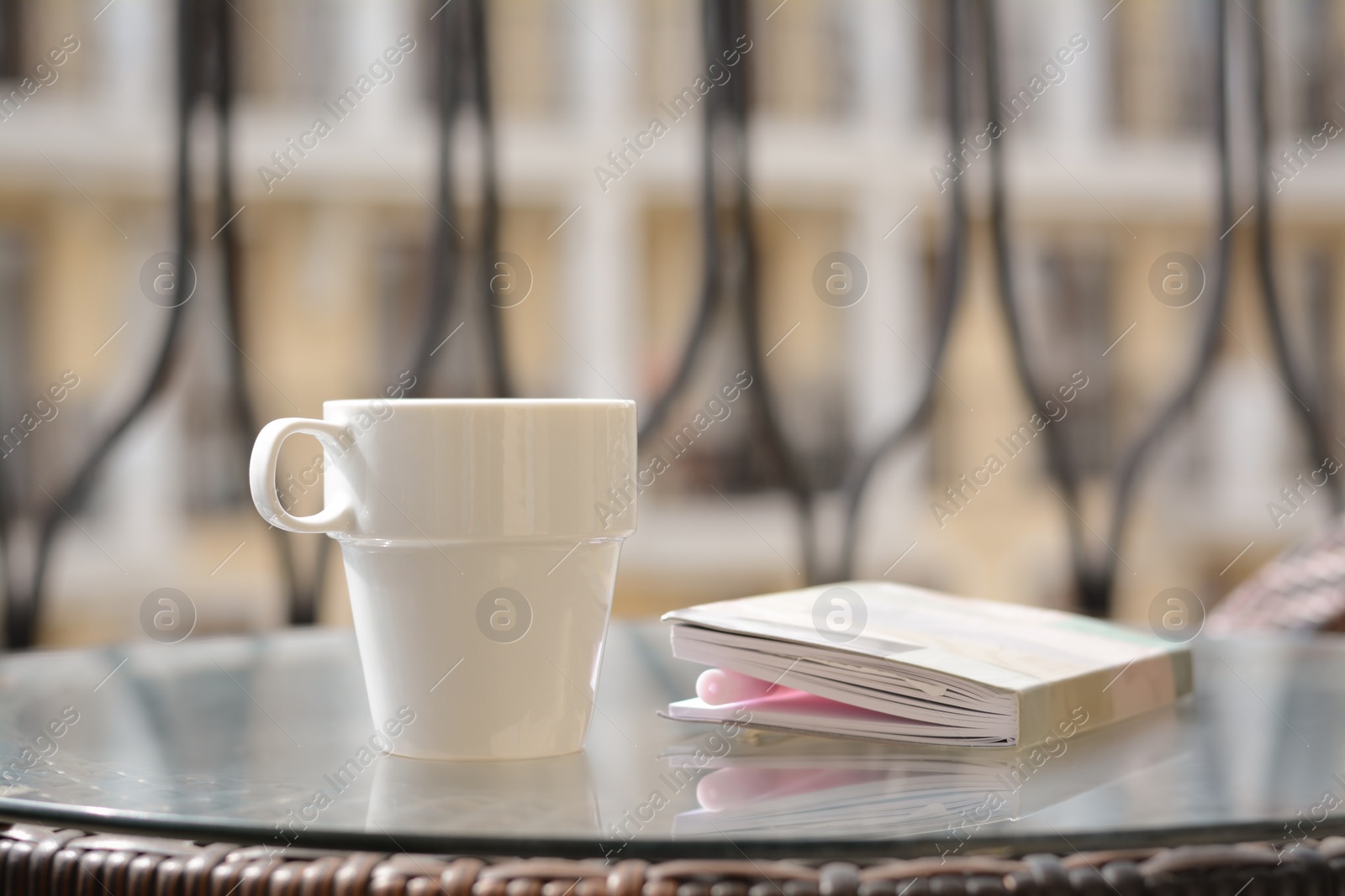 Photo of Ceramic cup of drink and notebook with pen on glass table outdoors. Good morning