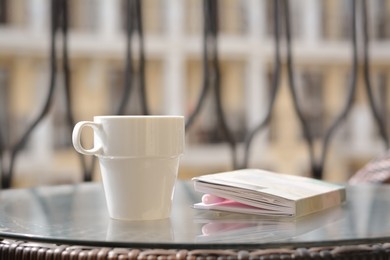 Ceramic cup of drink and notebook with pen on glass table outdoors. Good morning