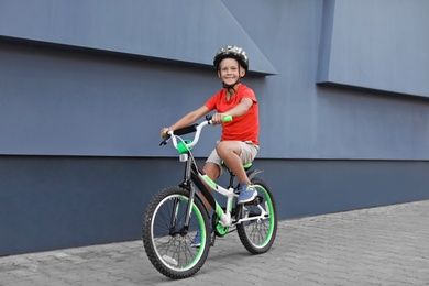 Little boy riding bicycle on street near gray wall