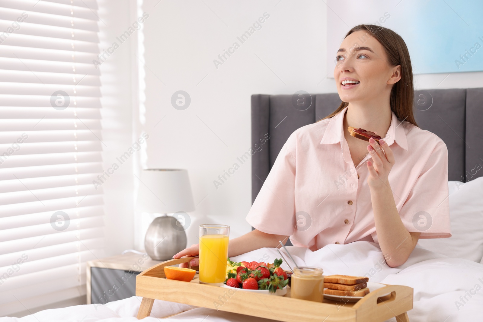 Photo of Smiling woman having breakfast in bed at home. Space for text