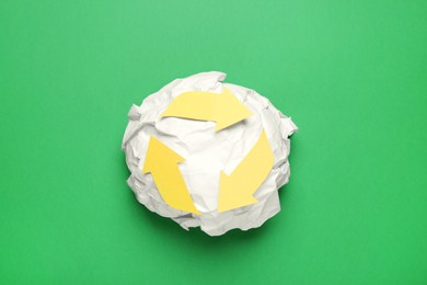 Photo of Crumpled paper with recycling symbol on green background, top view
