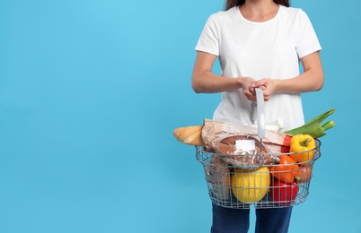 Photo of woman with shopping basket full of products on blue background, closeup. Space for text